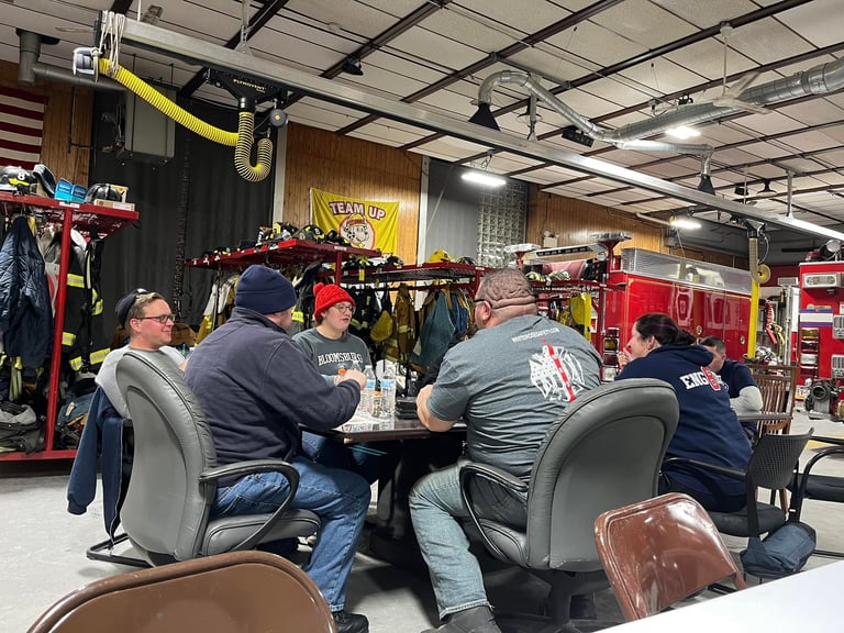 Group of people sitting at a table in a warehouse filled with firefighting equipment and gear displays