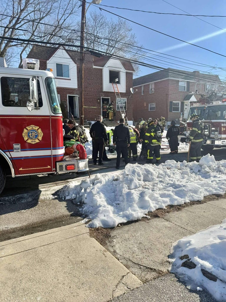 Fire truck and firefighters responding to residential street with brick homes and snow piles