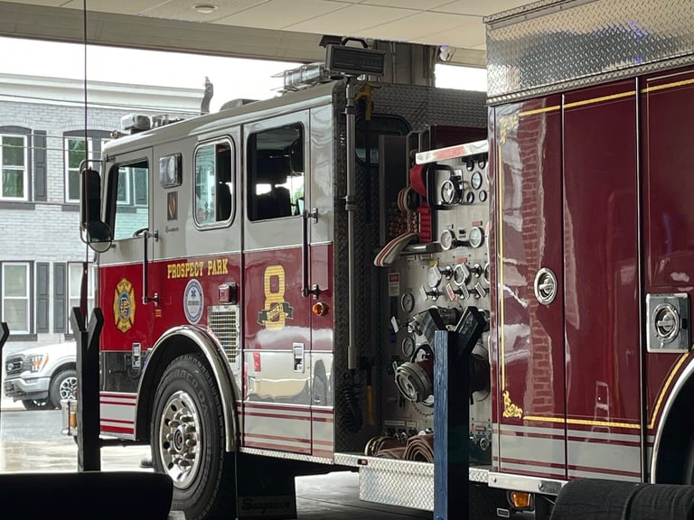 Red and white fire truck with open equipment compartment displaying tools and hoses parked indoors