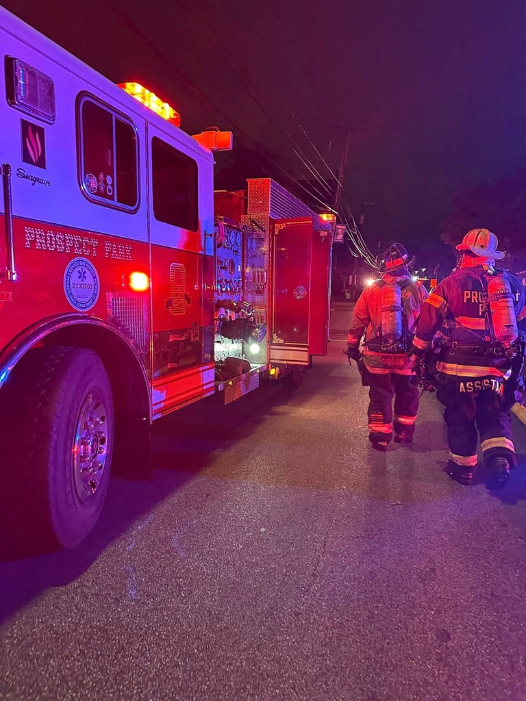 Firefighters in reflective gear standing near red fire trucks at night with emergency lights activated