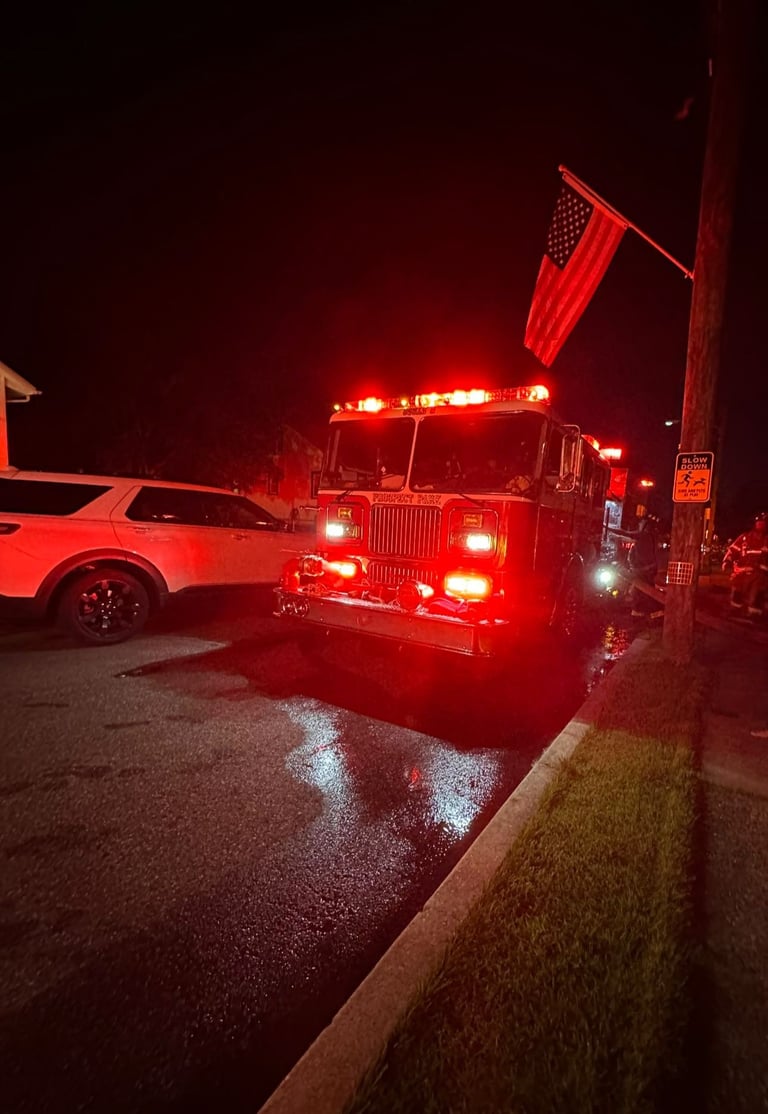 Fire truck with red emergency lights illuminated at night, parked near a building with wet pavement